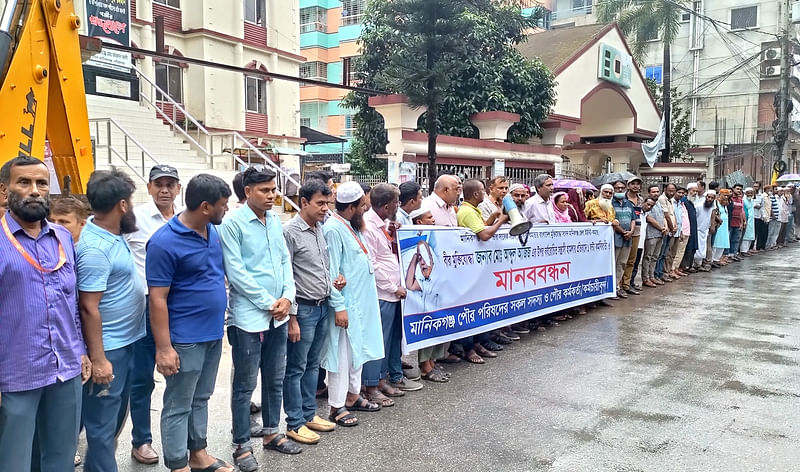 মানিকগঞ্জে বীর মুক্তিযোদ্ধার ওপর হামলার প্রতিবাদে মানববন্ধন করেন পৌরসভার সদস্য, কর্মকর্তা ও কর্মচারীরা। সোমবার দুপুরে জেলা শহরে পৌর ভবনের সামনে