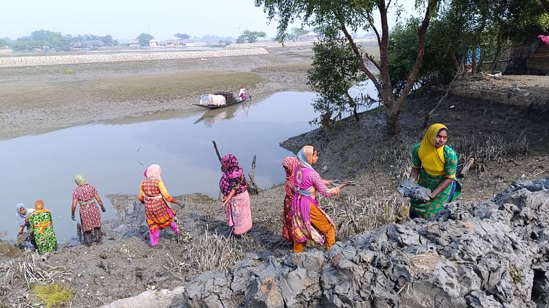 শীত উপেক্ষা করে মাটির দলা হাতে হাতে সড়কের ঢালে স্তূপ করে রাখছেন নারী শ্রমিকেরা। সোমবার সকাল সাড়ে সাতটার দিকে খুলনার কয়রা উপজেলার সুন্দরবনসংলগ্ন হায়াতখালী গ্রামের কয়রা নদীর চরে