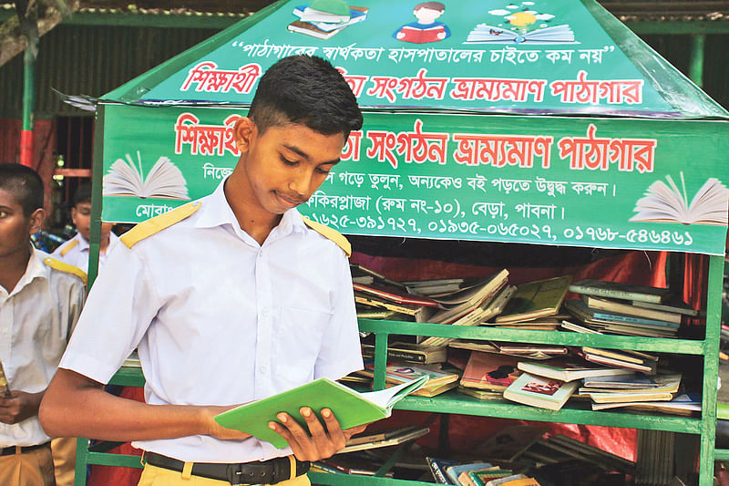 ভ্রাম্যমাণ পাঠাগার থেকে বই নিয়ে পড়ছে এক ছাত্র। সম্প্রতি বেড়ার আলহেরা একাডেমি স্কুল এন্ড কলেজ প্রাঙ্গণে।