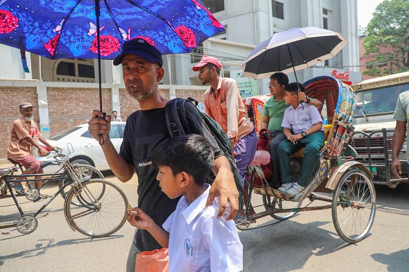 তীব্র গরমে ছাতা মাথায় শিশুকে স্কুল থেকে বাসায় নিয়ে যাচ্ছেন স্বজনেরা। লক্ষ্মীবাজার, ঢাকা, ২৮ এপ্রিল