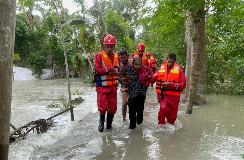 রিমালের প্রভাবে নদ-নদীর পানি বেড়ে লোকালয় ঢুকে পড়েছে। বৃদ্ধ এক নারীকে বাড়ি থেকে আশ্রয়কেন্দ্রে নিয়ে যাচ্ছেন রেড ক্রিসেন্টের স্বেচ্ছাসেবকেরা। শারিকতলা গ্রাম, পিরোজপুর