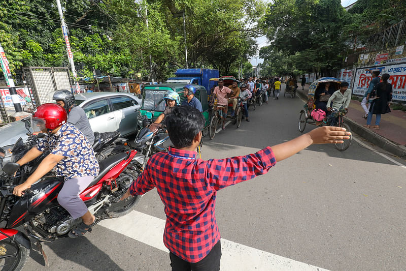 হাত ইশারায় আলাদা আলাদা লেনে যানবাহন চলাচল নিয়ন্ত্রণ করছেন একজন। নীলক্ষেত, ঢাকা