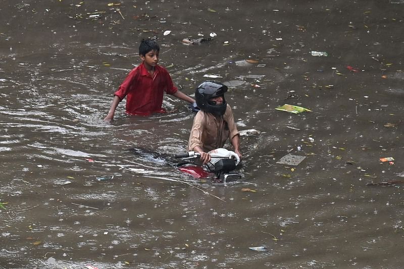 বৃষ্টি পানিতে ডুবে যাওয়া সড়কে অচল হয়ে পড়া মোটরসাইকেলকে টেনে নিয়ে যাচ্ছেন এক ব্যক্তি