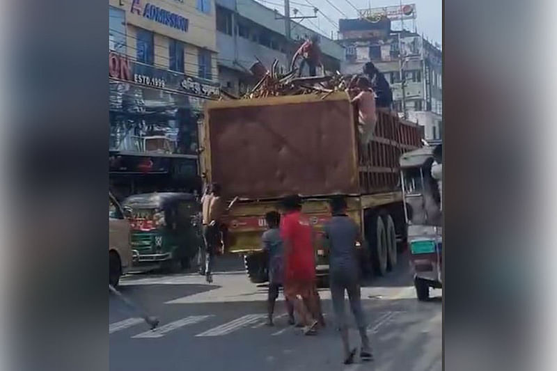 চট্টগ্রামের হালিশহরের বড়পোল এলাকায় চলন্ত ডাম্প ট্রাক থেকে ইস্পাতের কাঁচামাল পুরোনো লোহার টুকরো সরিয়ে নেওয়া হচ্ছে। সম্প্রতি তোলা একটি ভিডিও থেকে নেওয়া।