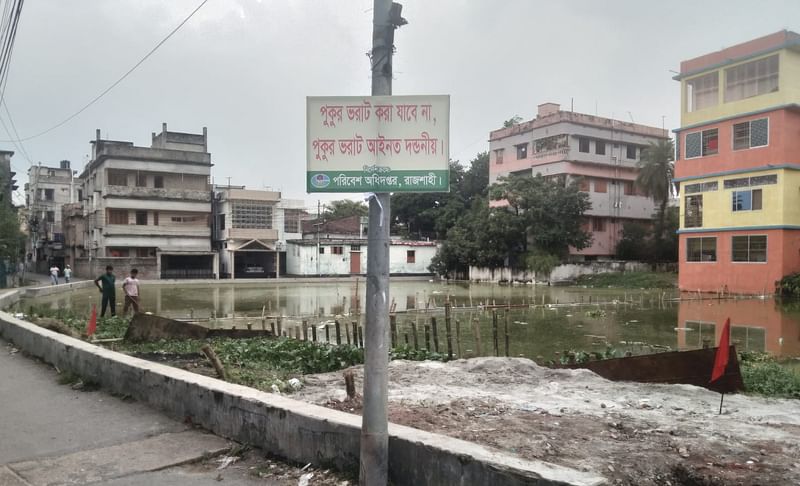 পুকুরটি ভরাট না করতে পরিবেশ অধিদপ্তরের সাইনবোর্ড। আজ সোমবার বিকেলে রাজশাহী নগরের আরাজি শিরোইল এলাকায়