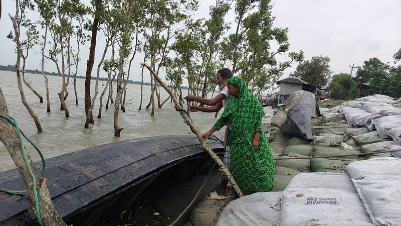 ক্ষতির হাত থেকে রক্ষা করতে ছোট ইঞ্জিনচালিত নৌকাটি বেঁধে রাখছেন শাহাদাৎ-ফরিদা দম্পতি। আজ বৃহস্পতিবার বিকেলে সাতক্ষীরার শ্যামনগর উপজেলার ভামিয়া এলাকায় খোলপেটুয়া নদীতীরে