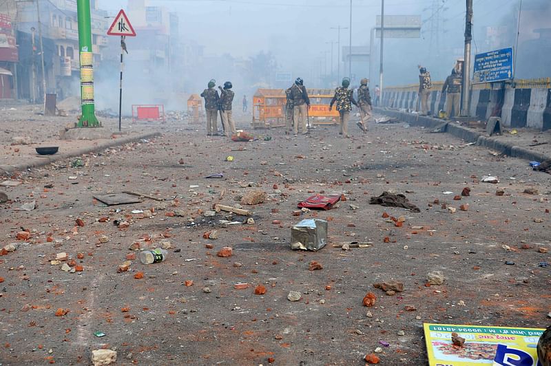 Policemen stand along a road scattered with stones as smoke billows from buildings following clashes between supporters and opponents of a new citizenship law, at Bhajanpura area of New Delhi on 24 February 2020, ahead of US President arrival in New Delhi. Photo: AFP