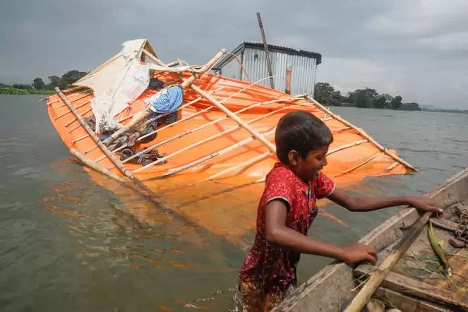 A child tries to jump on a boat as shops and structures go under water following water level rise in river Turag at Birulia, Savar on 9 August 2020.