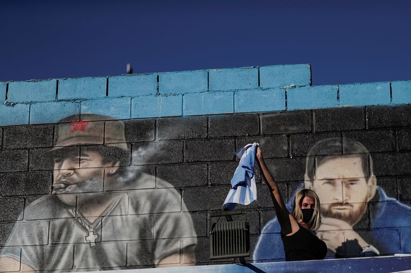 A woman reacts in front of a mural depicting the late football legend Diego Maradona and PSG player Lionel Messi near Bella Vista cemetery