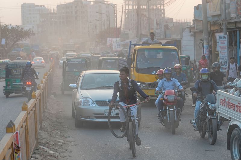 Commuters drive and ride on a road under heavy smog conditions in Dhaka