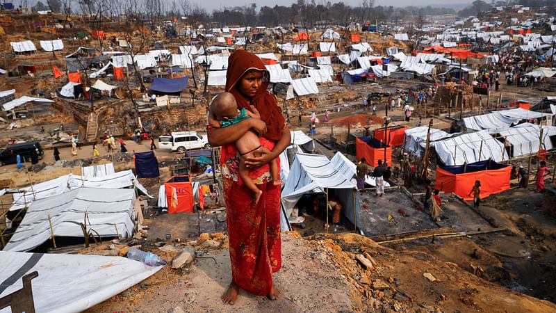 A Rohingya refugee woman carries her child as she looks on in a refugee camp after a massive fire broke out two days ago in Cox's Bazar, Bangladesh, on 24 March 2021