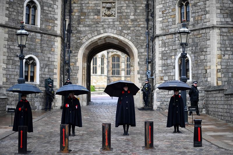 Wardens of the Castle shelter from the rain beneath umbrellas outside Windsor Castle in Windsor, west of London, on 10 April 2021, the day after the death of Britain's Prince Philip, Duke of Edinburgh, at the age of 99