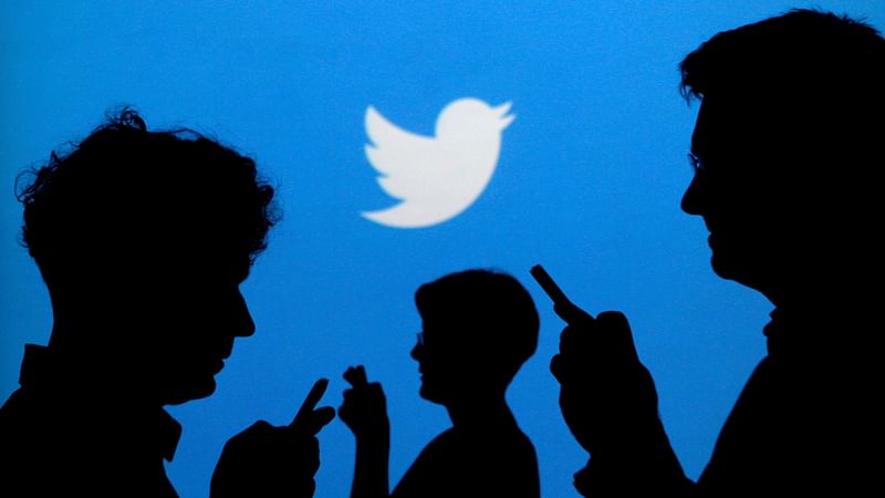 People holding mobile phones are silhouetted against a backdrop projected with the Twitter logo in this illustration picture taken on 27 September 2013