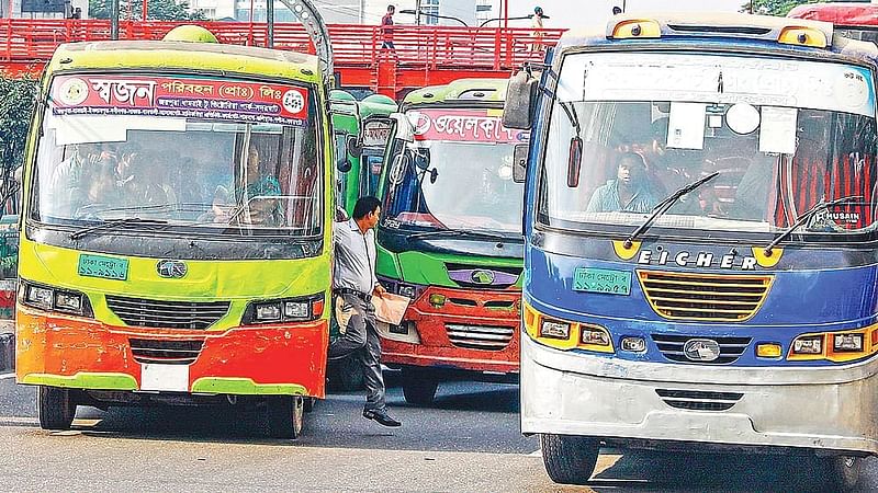 A man gets off a bus in the middle of the road with a moving bus in the back in Bangla Motor area in Dhaka.