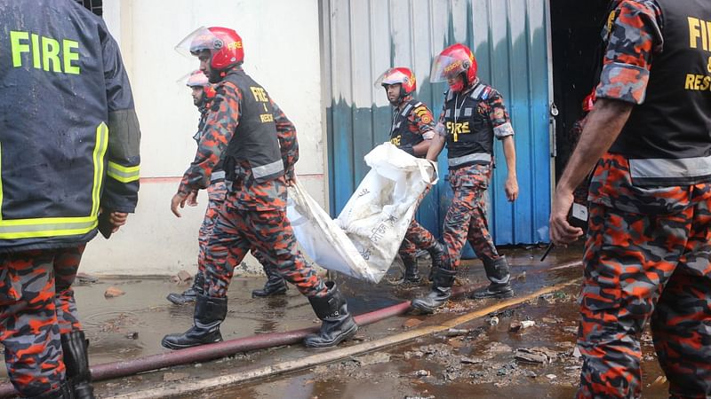 Fire service men carry remaining parts of a charred body in a bag as fire rages at a factory building of Hashem Food and Beverage Ltd. in Karnagop area of Rupganj in Narayanganj on 9 July 2021