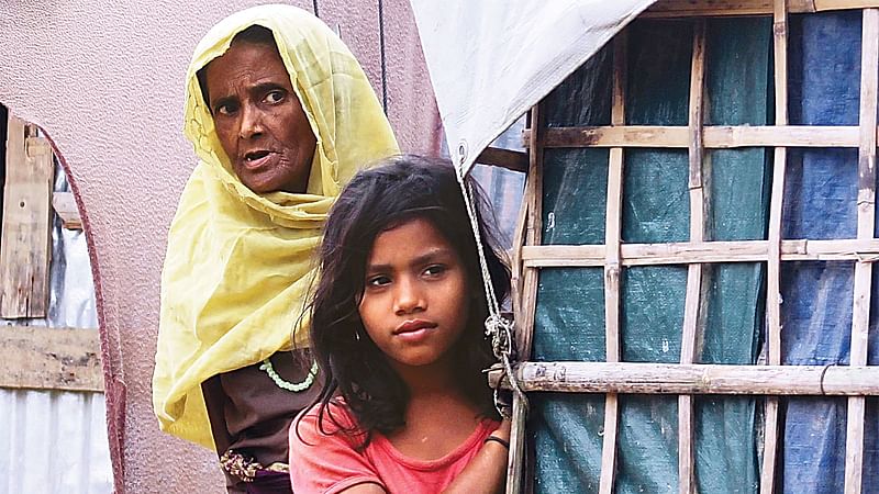 A Rohingya woman and a girl look from their camp-house