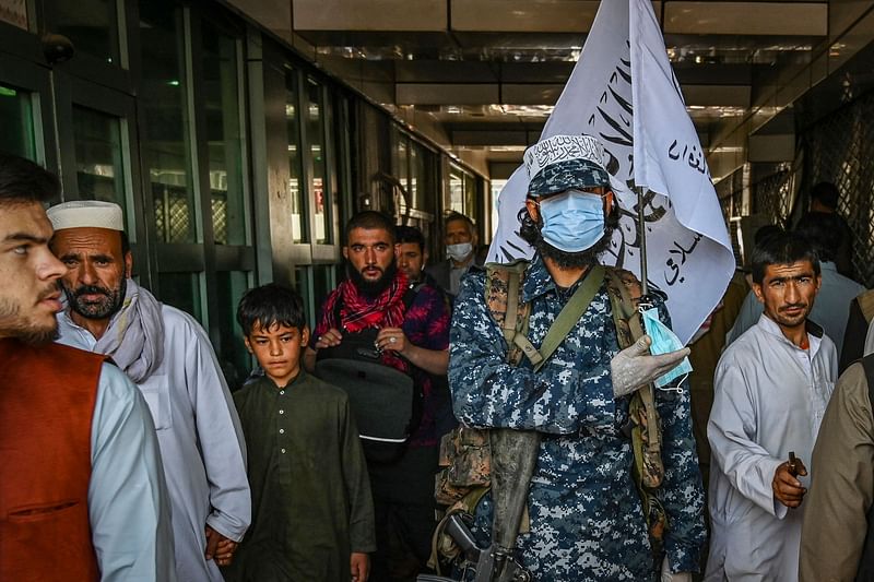 A Taliban fighter stands guard as people move past him at a market with shops dealing with currency exchange in Kabul on 5 September 2021