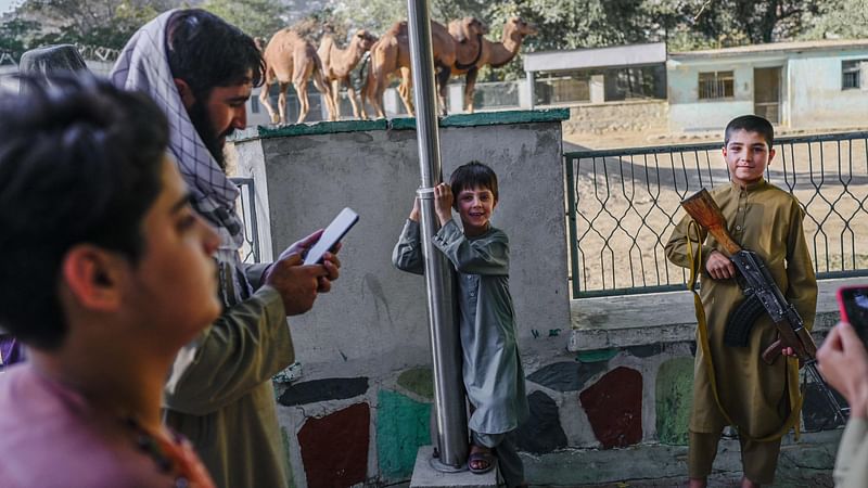 A boy poses for a picture with the rifle of a Taliban fighter near the camel enclosure at the Kabul zoo on 17 September, 2021