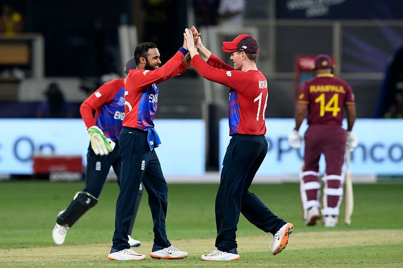 England's Adil Rashid (L) celebrates with his captain Eoin Morgan after taking the wicket of West Indies' Ravi Rampaul (R) during the ICC men’s Twenty20 World Cup cricket match between England and West Indies at the Dubai International Cricket Stadium in Dubai on October 23, 2021.