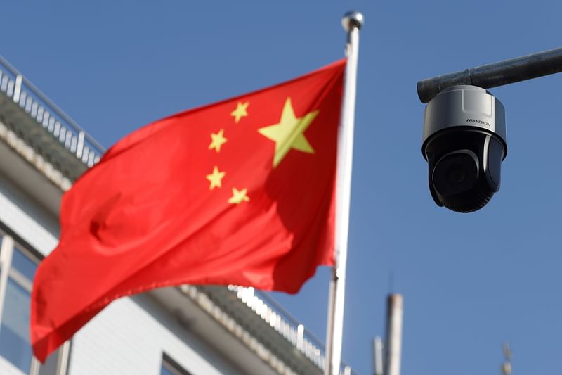 A security surveillance camera overlooking a street is pictured next to a nearby fluttering flag of China in Beijing, China on 25 November 2021.