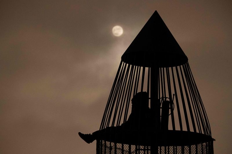 The moon shines though clouds as people sit inside a rocket ship-themed playground tower before a lunar eclipse on 18 November, 2021 in Torrance, California