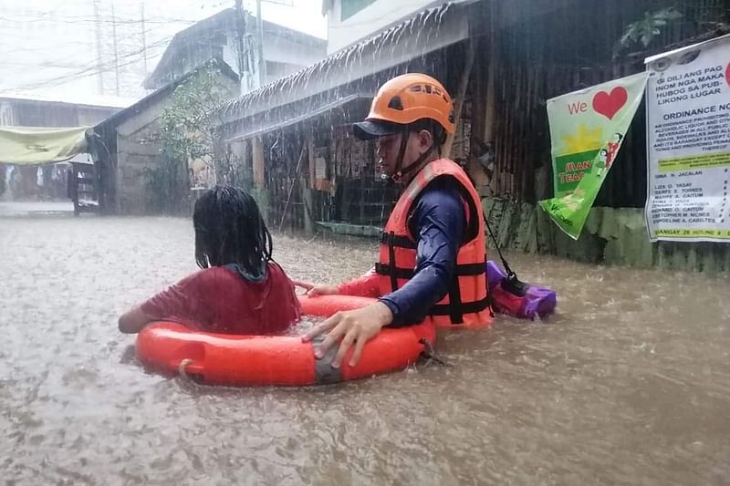 This handout photo taken and received on 16 December, 2021 from the Philippine Coast Guard (PCG) shows a Coast Guard member (R) assisting a flood-affected resident in a flotation ring during an evacuation from their homes next to a swollen river in Cagayan de Oro city on southern Mindanao island, amid heavy rains brought about by Typhoon Rai