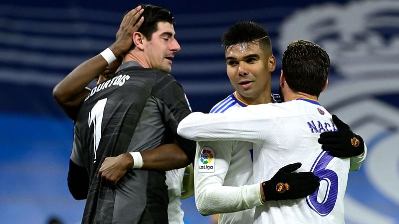 Real Madrid's Belgian goalkeeper Thibaut Courtois (L) and Real Madrid's Brazilian midfielder Casemiro celebrate with teammates at the end of the Spanish league football match between Real Madrid CF and Club Atletico de Madrid at the Santiago Bernabeu stadium in Madrid on 12 December, 2021