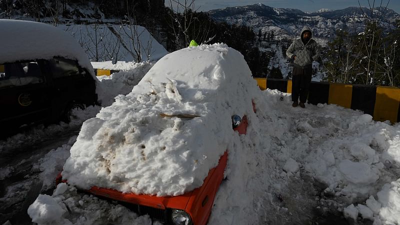 A man stands next to snow-covered card stucked on a road after a blizzard that started on January 7 and led to visitors being trapped in vehicles along the roads to the resort hill town of Murree, some 70 Kms northeast of Islamabad on 9 January, 2022