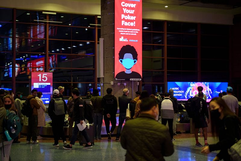 A sign reminds airline passengers to wear face masks as they wait to collect bags from a baggage carousel at the Harry Reid International Airport (LAS) on 2 January, 2022 in Las Vegas, California