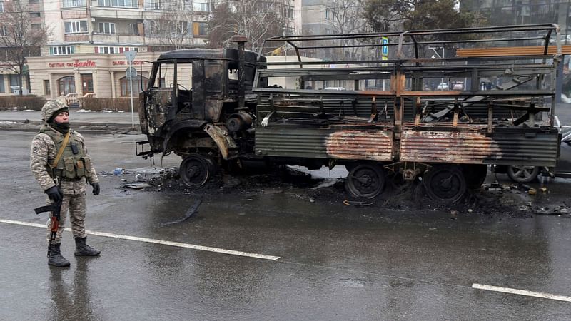 A Kazakh law enforcement officer stands guard near a burnt truck while checking vehicles in a street following mass protests triggered by fuel price increase in Almaty, Kazakhstan on 8 January, 2022