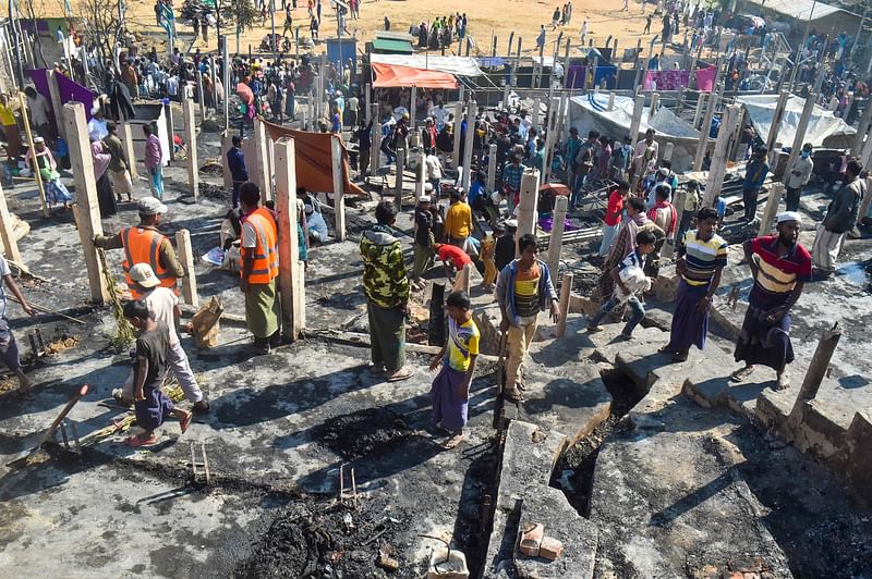 People gather on the ground of brunt-out houses a day after a fire gutted parts of a Rohingya refugee camp in Ukhiya on 10 January 2022