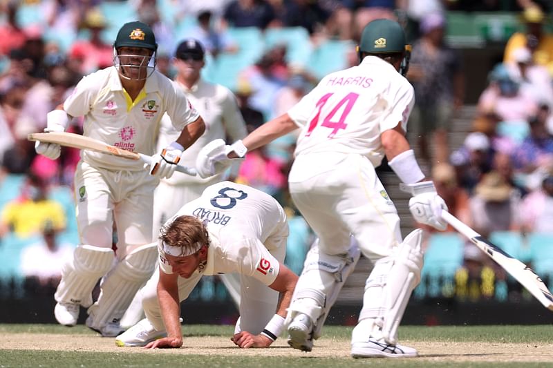 England's paceman Stuart Broad (C) dives in an attempt to filed on his own bowling as Australia's batman David Warner (L) and Marcus Harris run between the wickets on day four of the fourth Ashes cricket Test match between Australia and England at the Sydney Cricket Ground on 8 January, 2022