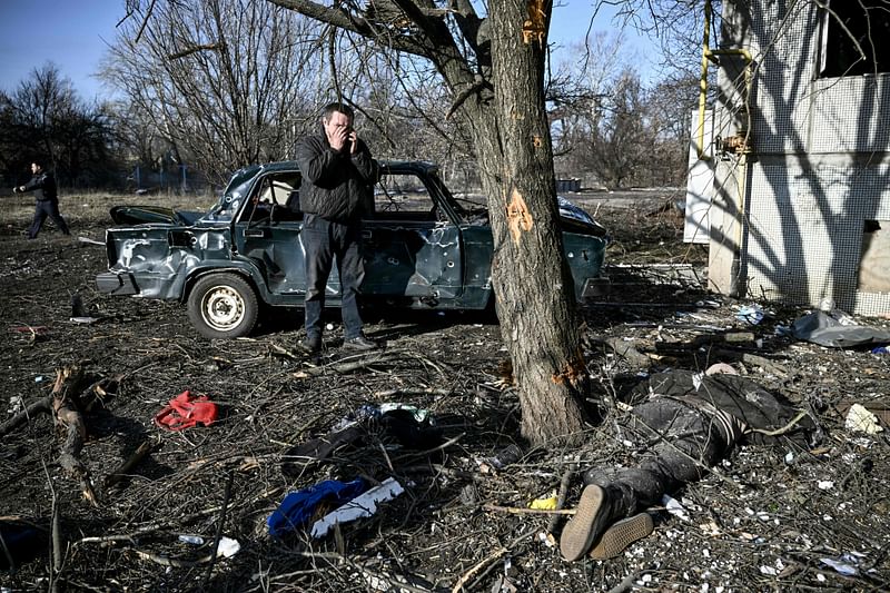 A man reacts on the phone as he stands by a body stretched out on the ground after bombings on the eastern Ukraine town of Chuguiv on 24 February, 2022, as Russian armed forces are trying to invade Ukraine from several directions, using rocket systems and helicopters to attack Ukrainian position in the south, the border guard service said