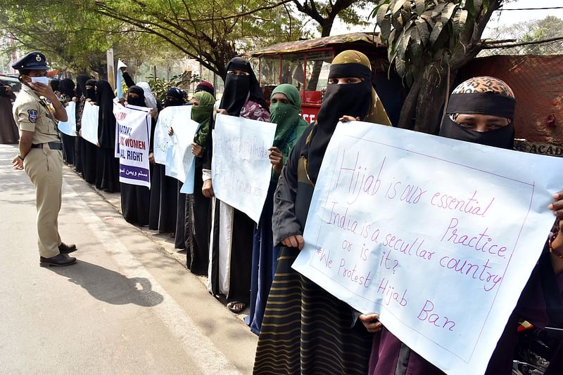 Police personnel stands guard as women and girls holding placards stage a peaceful protest over the hijab ban imposed in the few colleges in Karnataka, near Shanthi Nagar Hockey Stadium, in Hyderabad on 15 February