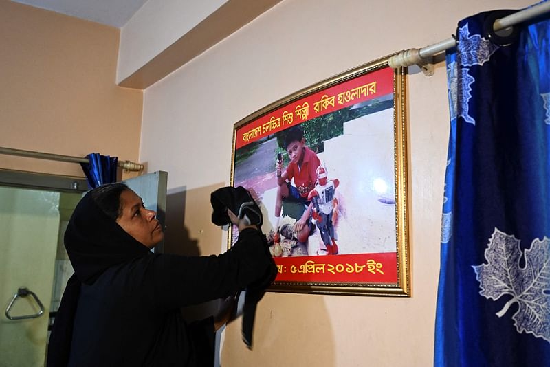 In this picture taken on 9 February 2022, Rita Begum, cleans a picture frame of her son Rakib Howlader, a 14-year-old boy who died during his arrest by the police in 2018, at her home in Dhaka