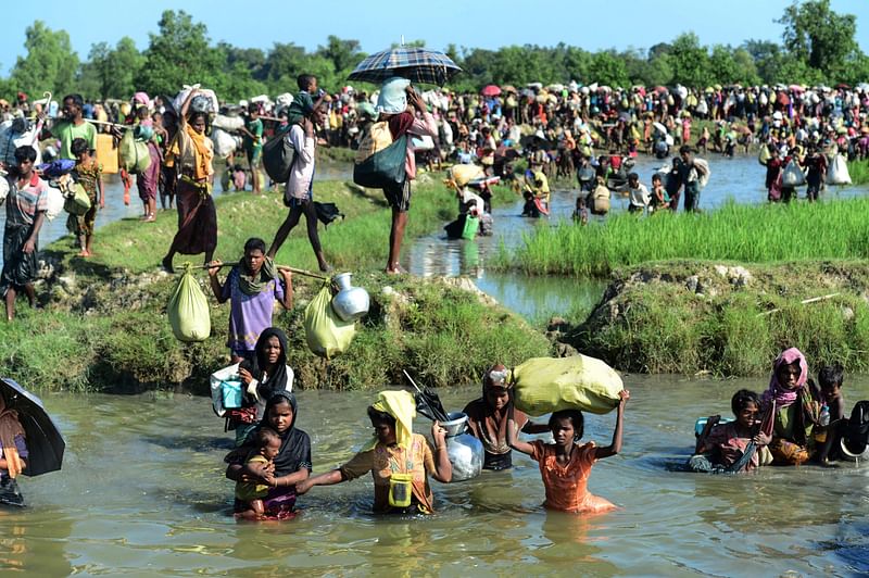 In this file photo taken on 16 October, 2017, Rohingya refugees walk through a shallow canal after crossing the Naf River as they flee violence in Myanmar to reach Bangladesh