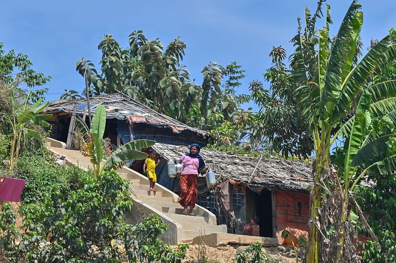 In this picture taken on 22 March 2022, a Rohingya refugee woman walks back to her home after collecting drinking water at Jamtoli refugee camp in Ukhiya