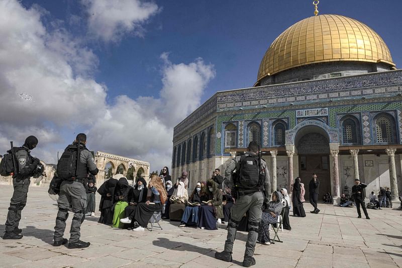 Israeli policemen stand guard in front of Muslim women praying in front of the Dome of the Rock mosque as a group of religious Jewish men and women visit the Temple Mount, which is known to Muslims as the Haram al-Sharif (The Noble Sanctuary), at the Aqsa mosques compound in the old city of Jerusalem on 20 April, 2022