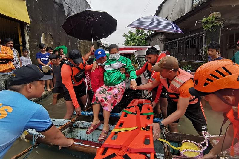 This undated handout photograph received from the Philippine Coast Guard (PCG) on 11 April, 2022 shows coast guard and police personnel evacuating a resident from a flooded area in Abuyog town