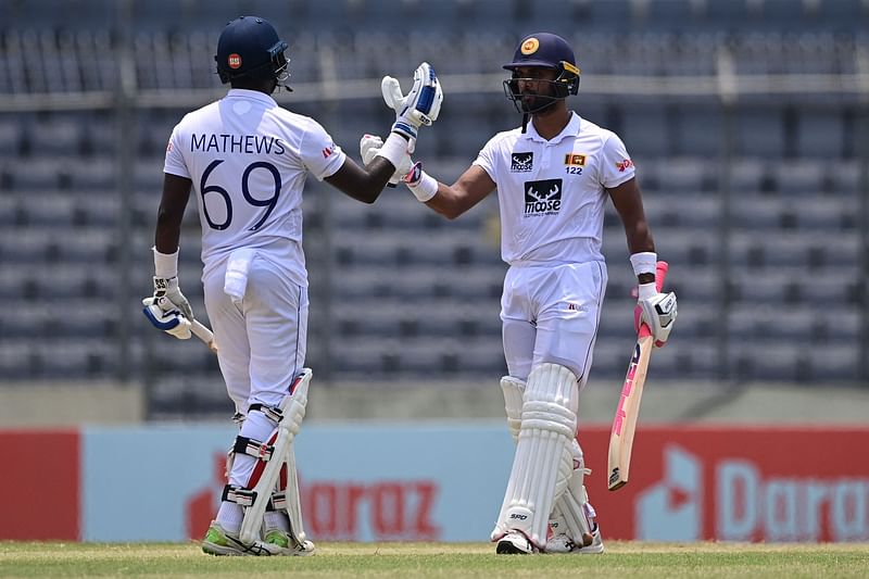 Sri Lanka's Dinesh Chandimal (R) celebrates after scoring a half century (50 runs) with teammate Sri Lanka's Angelo Mathews during the fourth day of the second Test cricket match between Bangladesh and Sri Lanka at the Sher-e-Bangla National Cricket Stadium in Dhaka on 26 May, 2022