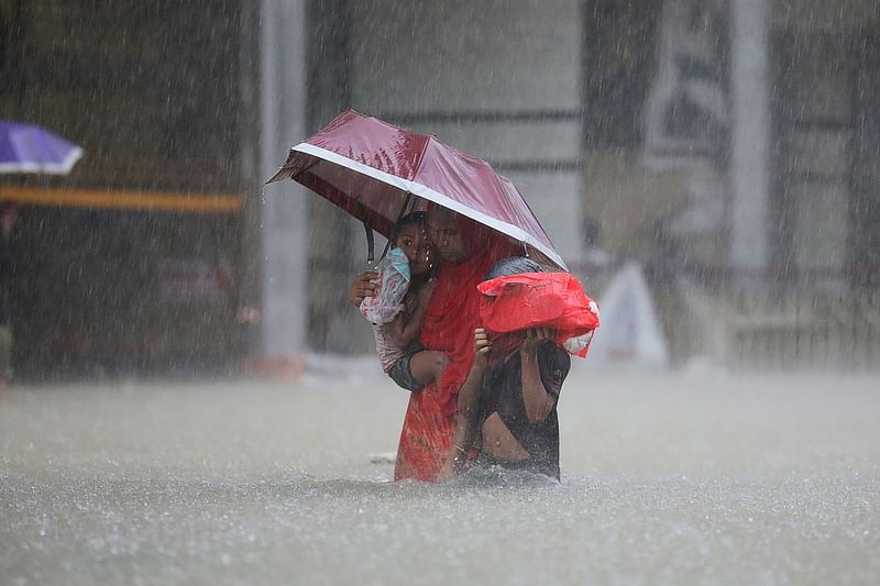 A woman with children wades through the water on a flooded street during the monsoon rains in Sylhet on 18 June 2022