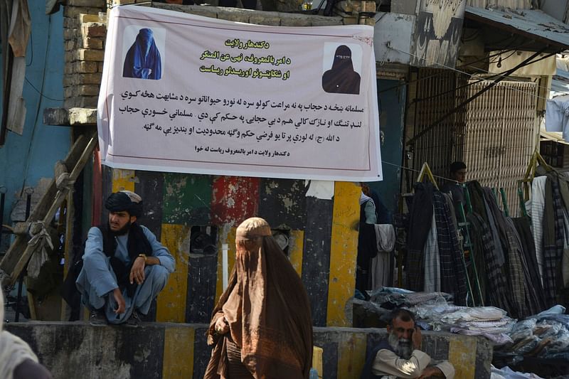 Burqa-clad women stand near a banner placed by Taliban authorities asking women to wear a hijab, in Kandahar on 16 June, 2022