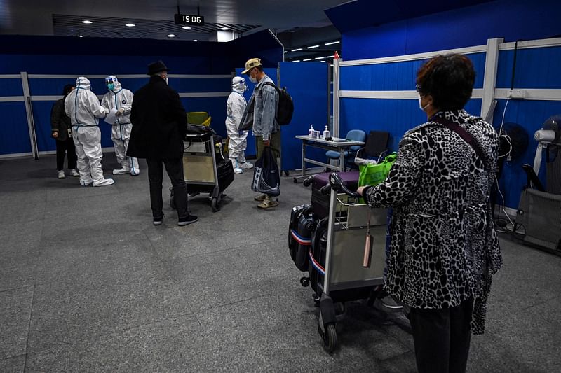 This file photo taken on 18 January, 2022 shows passengers, some wearing full personal protective equipment, waiting to be transported by bus to their quarantine hotels, after arriving at Pudong International Airport in Shanghai