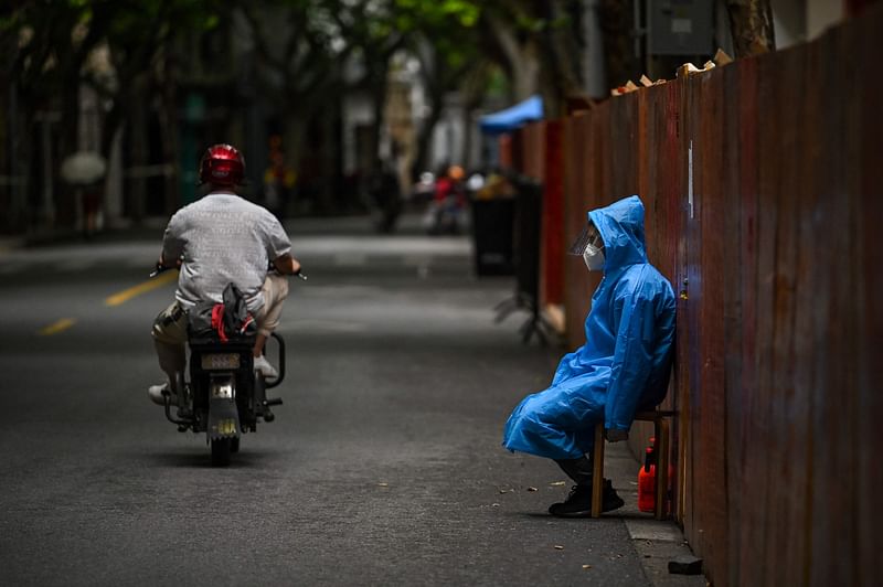 A worker sits next to a fence erected to close a residential area under Covid-19 lockdown in the Huangpu district of Shanghai on 10 June 2022