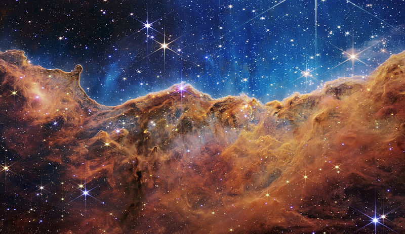 The "Cosmic Cliffs" of the Carina Nebula are seen in an image divided horizontally by an undulating line between a cloudscape forming a nebula along the bottom portion and a comparatively clear upper portion, with data from NASA's James Webb Space Telescope, a revolutionary apparatus designed to peer through the cosmos to the dawn of the universe and released on 12 July 2022.