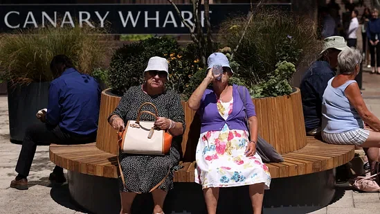 Women rest on a bench and drink water in hot weather during lunch hour in the financial district of Canary Wharf in London, Britain.