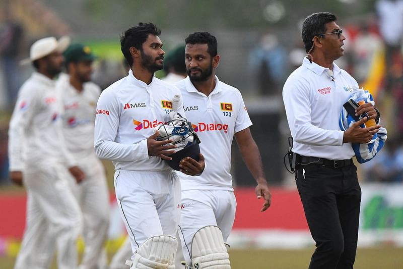 Sri Lanka's Dhananjaya de Silva and captain Dimuth Karunaratne (C) walk back to the pavilion as the match gets delayed due to bad light during the third day of the second Test between Sri Lanka and Pakistan at the Galle International Cricket Stadium in Galle on 26 July, 2022