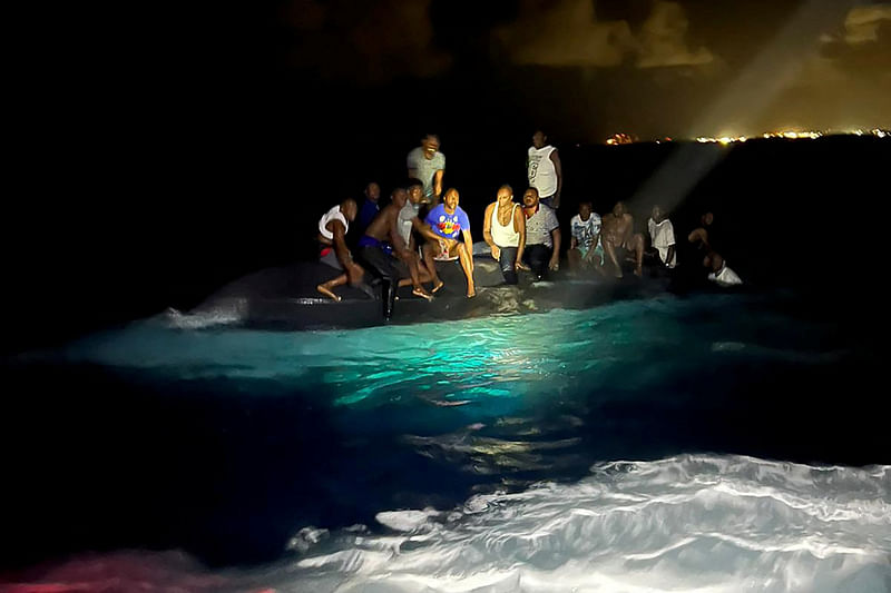 Survivors of a migrant boat that capsized perch on the overturned vessel off the coast of New Providence island, Bahamas 24 July , 2022