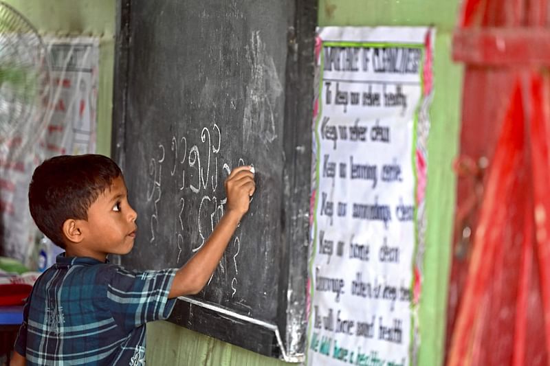 In this picture taken on 10 August, 2022, a Rohingya refugee child writes Rohingya language on a blackboard at a school in Kutupalong refugee camp in Ukhia