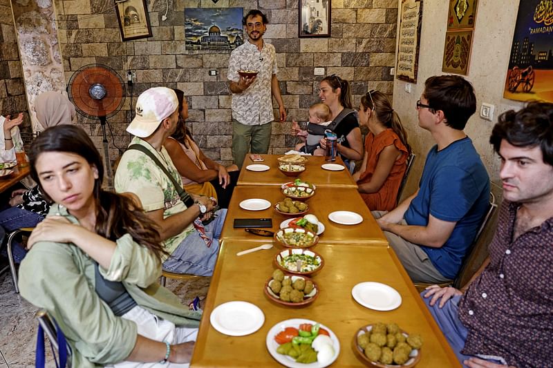 Tourguide Izzeldin Bukhari (C), who runs Jerusalem food tours and cooking classes, presents dishes to tourists in a restaurant during a guided tour in the Old City of Jerusalem on 26 July, 2022